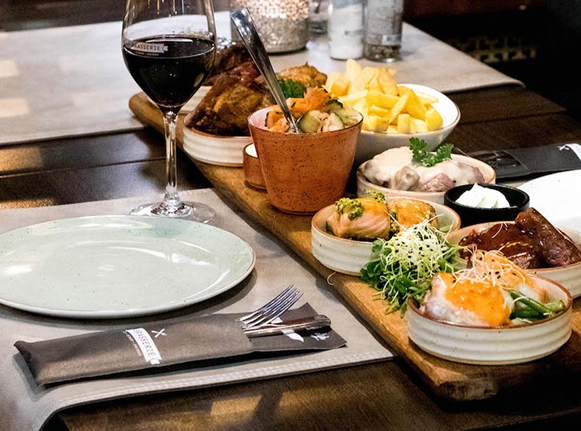 een bedekte tafel met diverse kleine gerechten waaronder patat en een salade en een bord met daarnaast een bedrukte bestekzak